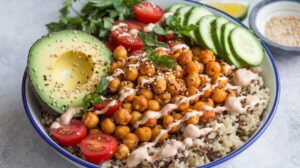 A vibrant Buddha bowl with crispy roasted chickpeas, quinoa, avocado, cherry tomatoes, cucumber slices, and a drizzle of creamy dressing.